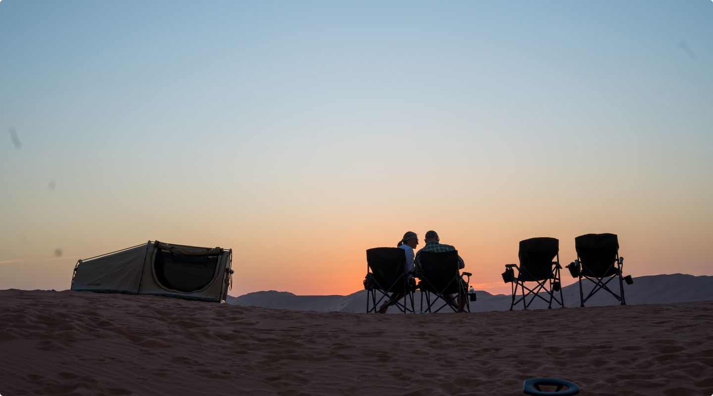 two people sat on chairs in the desert watching the sunset